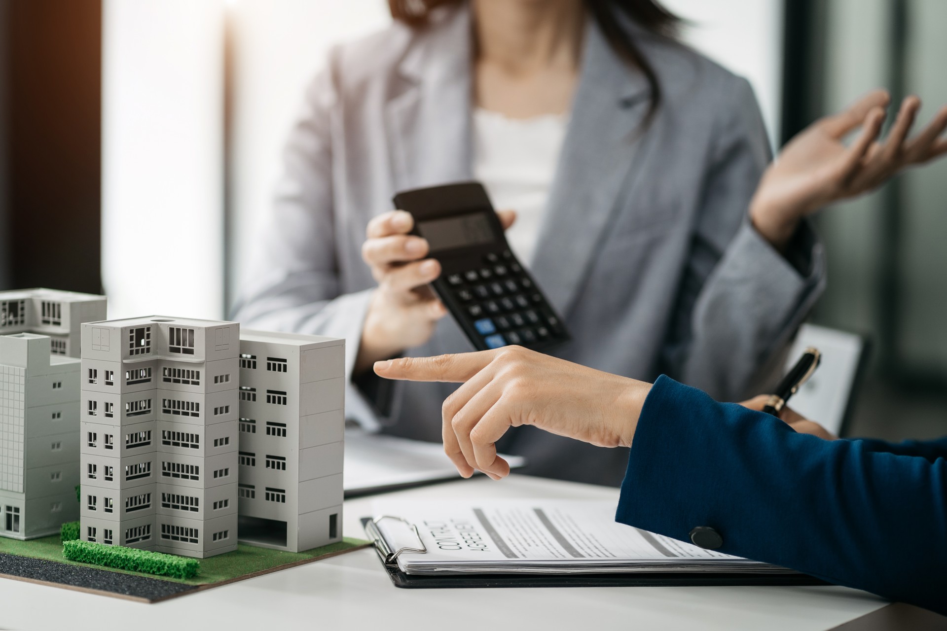 El oficial de préstamos hipotecarios utiliza una calculadora con un plano de casa sobre una mesa de madera.